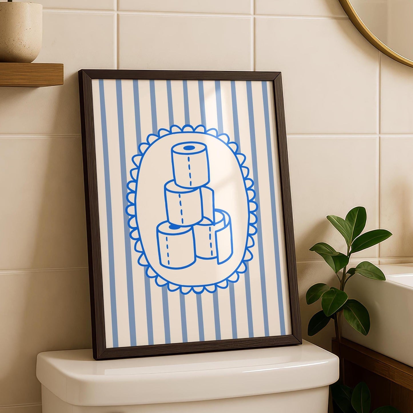 A framed print with a dark wood frame, depicting a stack of four toilet paper rolls in blue outline on a white oval, set against a background of light blue and white vertical stripes, sitting on a toilet tank.