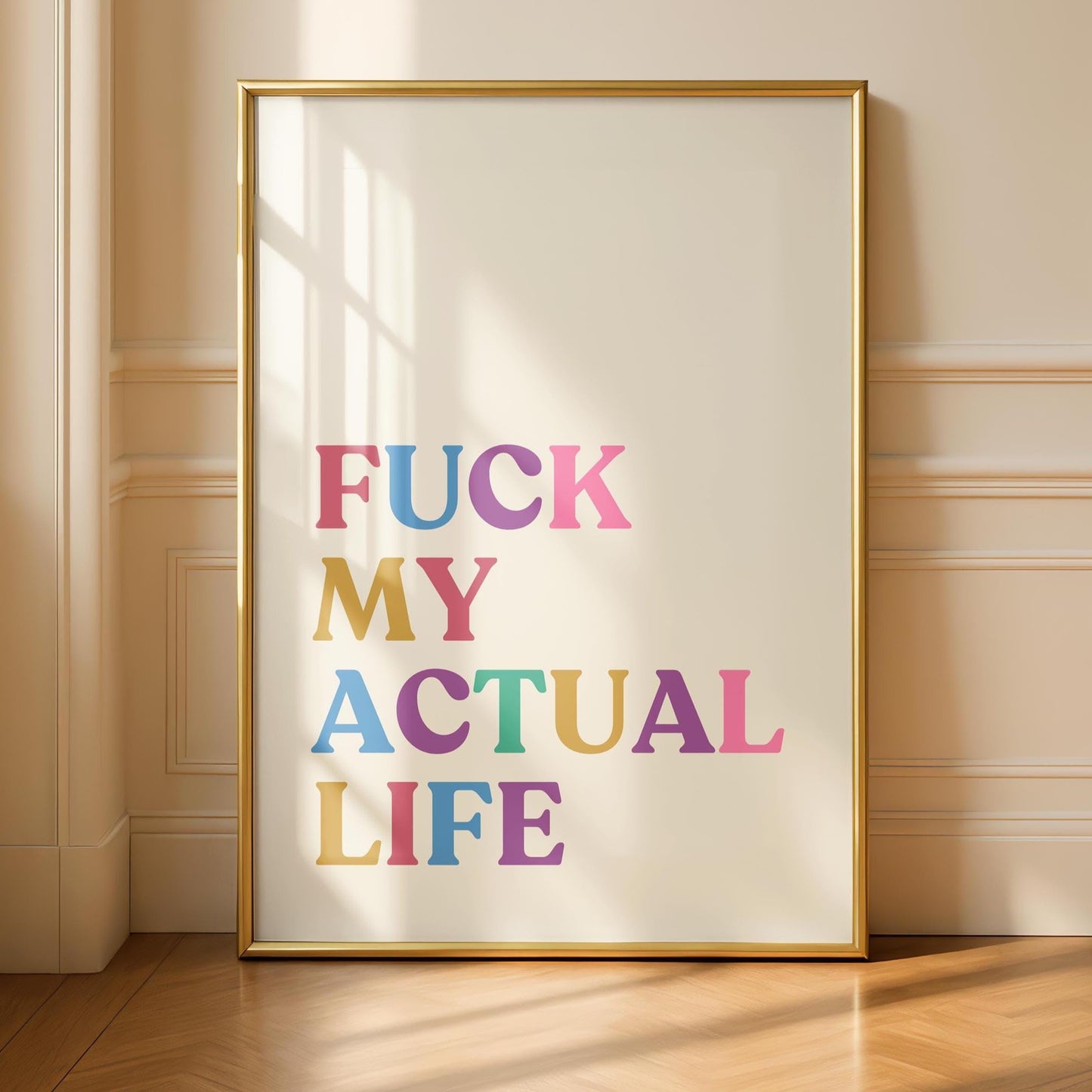 A gold-framed print on a light wall, reading "FUCK MY ACTUAL LIFE" in colorful, block letters, casting a shadow on the wall and floor.