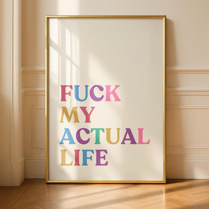 A gold-framed print on a light wall, reading "FUCK MY ACTUAL LIFE" in colorful, block letters, casting a shadow on the wall and floor.