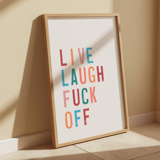 A framed print with the words "LIVE LAUGH FUCK OFF" in colorful, distressed block letters, leaning against a beige wall with a shadow cast upon it.