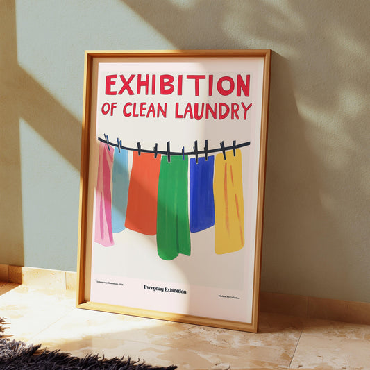 A framed poster with a white background depicts colorful clothes hanging on a clothesline, with red text reading "EXHIBITION OF CLEAN LAUNDRY."