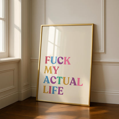 A gold-framed print on a light wall, reading "FUCK MY ACTUAL LIFE" in colorful, block letters, with sunlight streaming in from a window on the left.