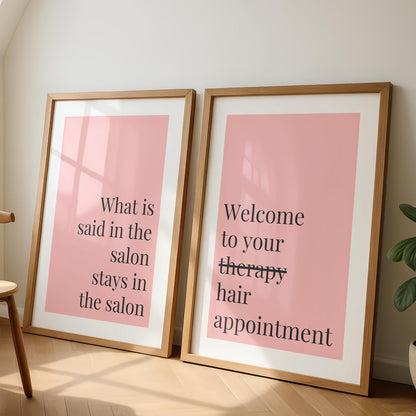 Two framed prints with pink backgrounds and black text lean against a white wall; the left reads "What is said in the salon stays in the salon," and the right reads "Welcome to your therapy hair appointment."