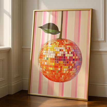 A gold-framed print of an orange disco ball with a green leaf, on a pink and beige striped background, leaning against a white wall and dark wood floor.