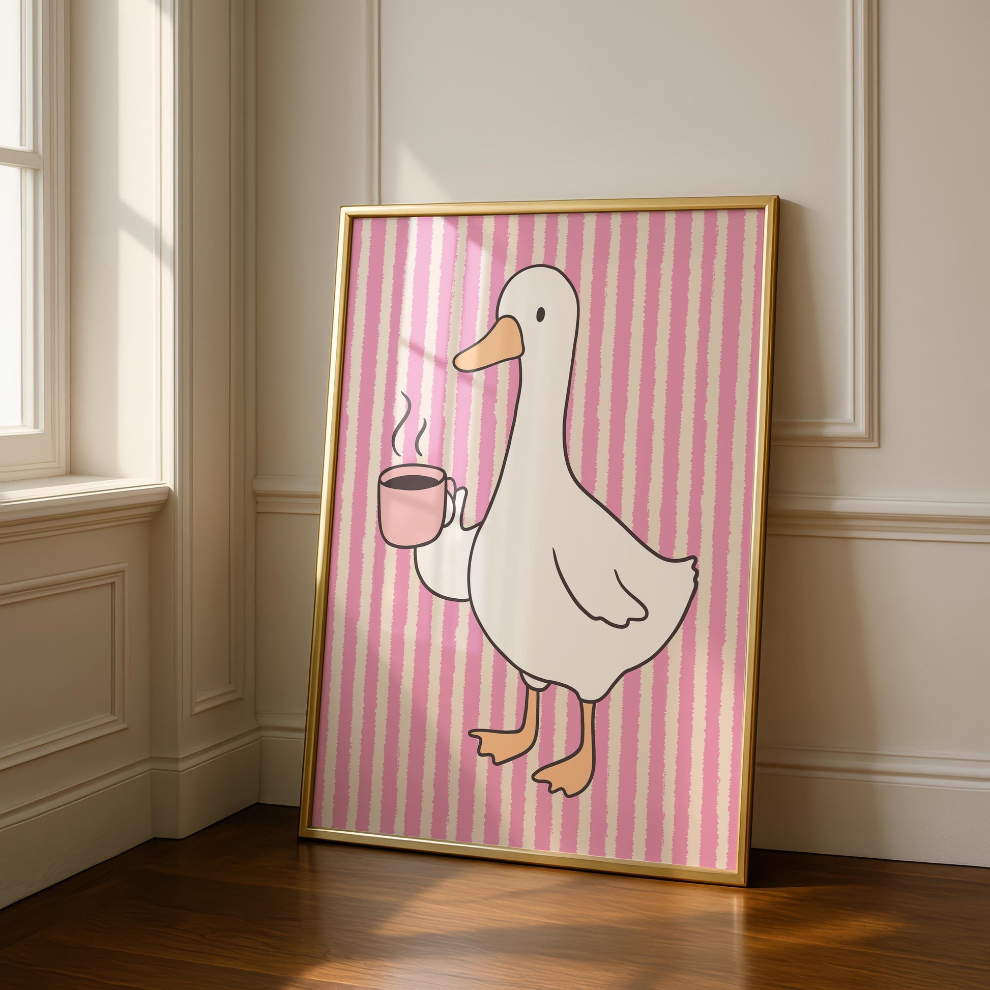A framed print of a white goose holding a pink coffee cup with steam, on a pink and white striped background, leaning against a white wall and wooden floor.
