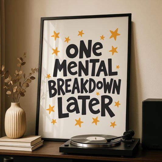 A black-framed print with "ONE MENTAL BREAKDOWN LATER" in black text and yellow stars on a cream background, leaning against a wall next to a beige vase and a record player.