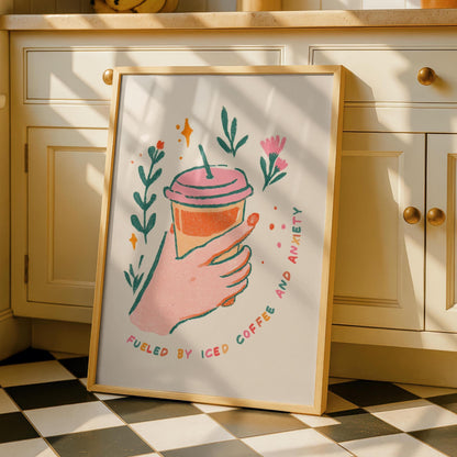 A framed print on a kitchen counter shows a hand holding an iced coffee with the text "FUELED BY ICED COFFEE AND ANXIETY" surrounded by green leaves and pink flowers.
