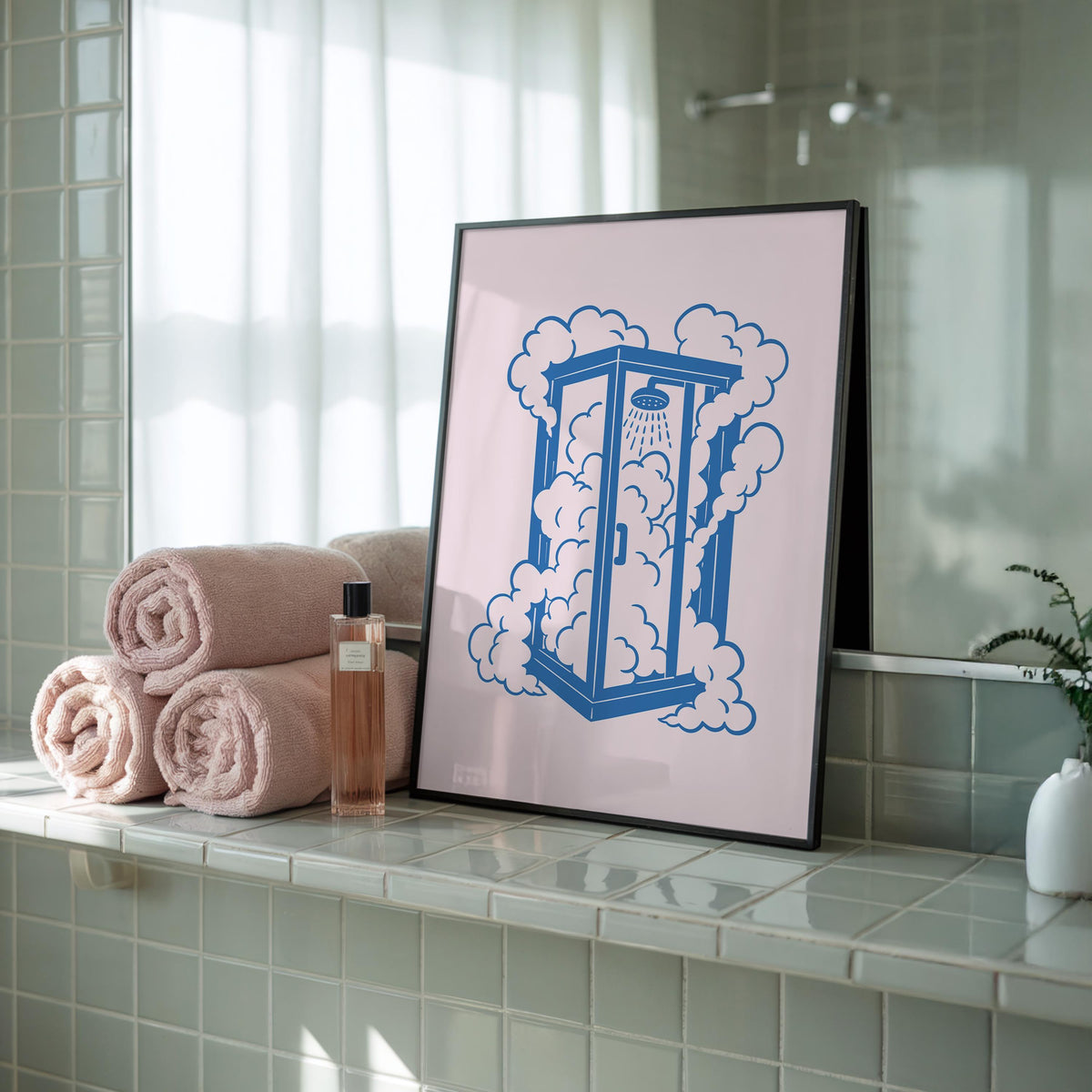 A black-framed print of a blue shower stall with pink clouds on a light pink background, leaning against a bathroom wall next to rolled towels and a bottle.